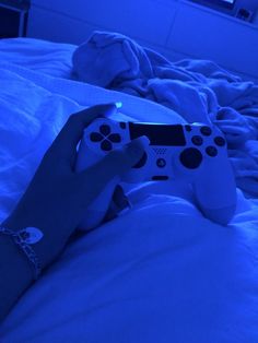 a person holding a video game controller in their hand on a bed with white sheets