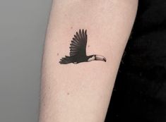 a black and white bird tattoo on the left arm with an arrow in it's beak