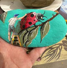 a hand holding a painted rock with a ladybug on it