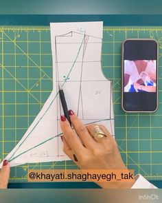 a person cutting out a pattern on a piece of paper with a cell phone next to it