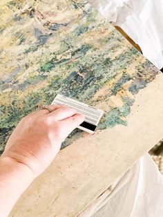 a person holding a piece of paper in front of a painting on a table top