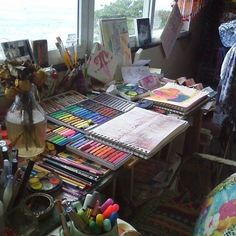 a desk with lots of art supplies on it and a large window in the background