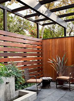 an outdoor patio with two chairs and a planter in the center, next to a wooden fence