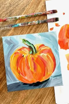 an orange painted pumpkin sitting on top of a wooden table next to paintbrushes