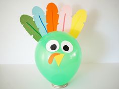 a green balloon with a fake turkey on it's head and feathers sticking out of the top