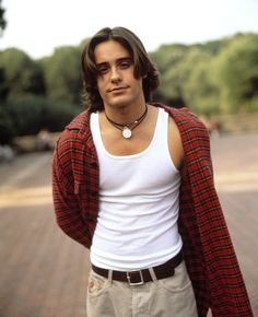 a man with long hair wearing a white tank top and red plaid cardigan jacket