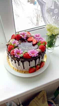 a chocolate cake with strawberries and flowers on the top is sitting next to a window