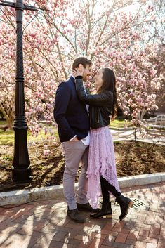 a man and woman standing next to each other in front of trees with pink flowers