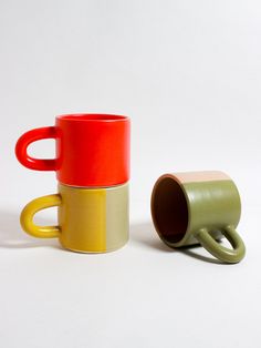 two coffee mugs sitting next to each other on a white surface with one red and one yellow