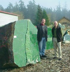 two men standing next to a large green rock