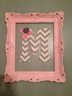 the letter m is decorated with flowers in a pink frame on a wall above a mirror