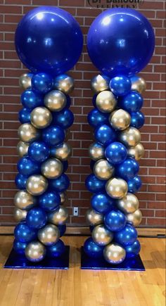 two tall blue and gold balloons are in front of a brick wall