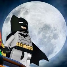 a lego batman standing on top of a roof in front of the moon with his caped head down