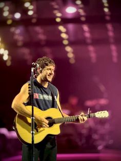 a man holding a guitar while standing in front of a microphone on top of a stage