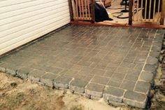 a brick patio with a wooden gate on the side and a dog laying in the back yard