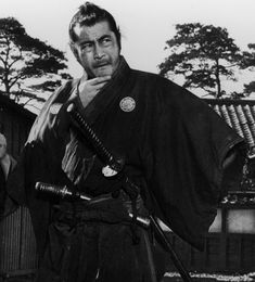 two men in traditional japanese garb holding swords and looking at the camera with trees in the background