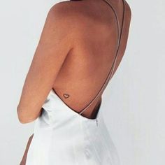 the back of a woman's white dress with a heart tattoo on her left shoulder