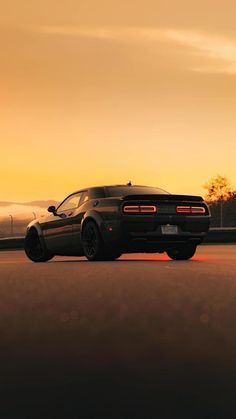 a black sports car is parked on the side of the road in front of an orange sunset