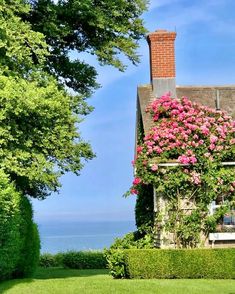 a house with pink flowers growing on it's roof next to some hedges and trees