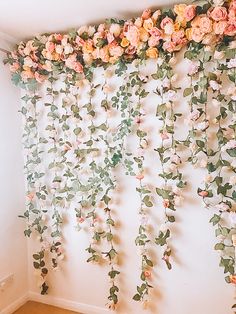 the wall is covered with pink flowers and greenery hanging from it's sides