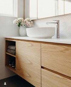 a bathroom sink sitting under a mirror next to a wooden cabinet with flowers in it