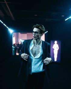 a man standing in the middle of a dark room with his shirt open and wearing glasses