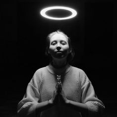 a woman standing in front of a black background with a halo above her head and hands clasped