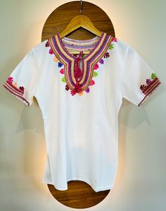 Introducing our exquisite Vintage Mexican Huipil blouse, a vibrant testament to the rich cultural heritage and artisanal mastery of Puebla, Mexico. Handcrafted with meticulous care by skilled artisans from indigenous communities, each Huipil is a unique embodiment of traditional craftsmanship and contemporary flair. Adorned with multicolored embroidery, every stitch tells a story, weaving together centuries of Mexican artistry into a breathtaking tapestry of color and design. Sourced directly from artisan communities, this Huipil captures the essence of Mexican tradition while celebrating the ingenuity of local designers. Designed to embrace the body in relaxed elegance, our Huipil boasts a loose-fitting silhouette that effortlessly flatters Small to Large sizes, ensuring a comfortable and Indigenous Mexican Clothing, Traditional Blouse For Navratri Rituals, Traditional Festive Blouse For Rituals, White Traditional Tops With Traditional Patterns, Traditional Multicolor Cotton Embroidered Top, Bohemian Multicolor Embroidered Festive Top, Traditional Embroidered Summer T-shirt, Traditional White Top With Intricate Embroidery, Multicolor Floral Embroidered Top For Navratri