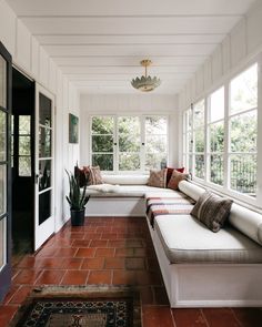 a long white couch sitting under two windows next to a rug and potted plant