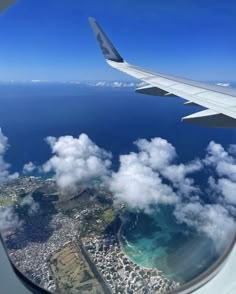 an airplane wing flying over the ocean and clouds