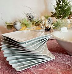 a stack of white plates sitting on top of a red table cloth next to a bowl