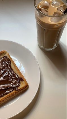 a piece of toast with chocolate spread on it next to a glass of ice coffee