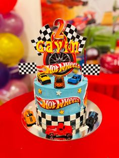 a birthday cake with cars on it sitting on top of a red table next to balloons