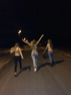 three women standing on the side of a road at night with their arms in the air