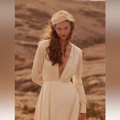 a woman wearing a white dress and veil in front of a desert landscape with flowers