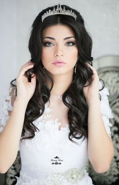 a woman wearing a tiara and holding her hair in one hand while looking at the camera