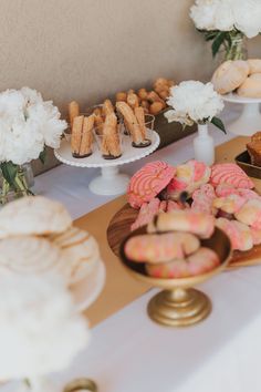 desserts and pastries are displayed on a white tablecloth with flowers in vases