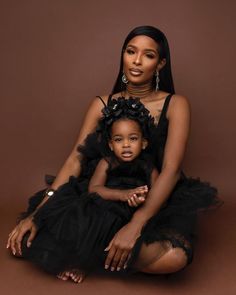 a woman sitting on the ground with a child in her lap and wearing a black dress