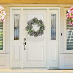 a white front door with two wreaths on the side and pink flowers hanging above it