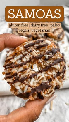 a person holding up a chocolate covered donut with coconut flakes on the top