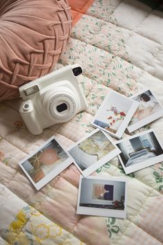 a camera and some polaroid pictures on a bed with a pillow in the background