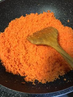 a wooden spoon in a black bowl filled with orange colored powdered food mixtures