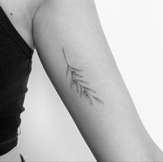 a black and white photo of a woman's arm with a small branch tattoo on it