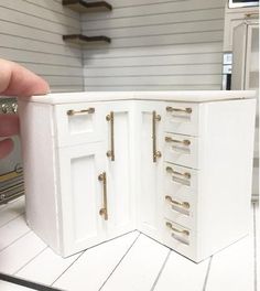 a hand is holding a miniature white cabinet