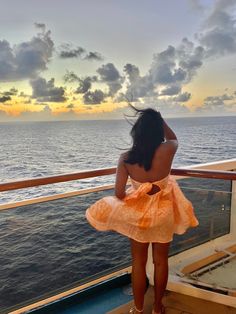 a woman in an orange dress looking out at the ocean