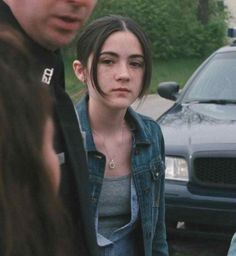 a young woman standing next to a man in front of a police car and talking on the phone