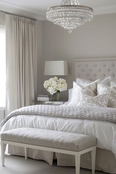 a white bed sitting under a chandelier next to a window