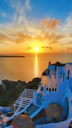 the sun is setting over an ocean with white buildings and straw umbrellas in front of it