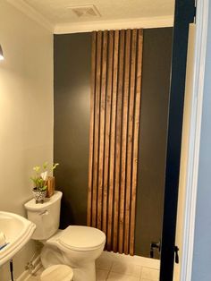 a white toilet sitting next to a bathroom sink under a window with wooden slats on it