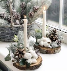 two candles sitting on top of a window sill with cotton balls and pine cones